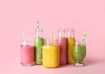 Glasses and bottles of different tasty smoothie with straws on pink background