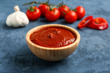 Bowl with tasty tomato paste, garlic and fresh vegetables on blue grunge background