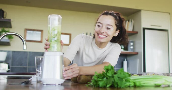 Happy biracial woman using blender, preparing smoothie in kitchen