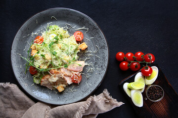 Fresh caesar salad in a white plate on a dark wooden table. Salad with chicken. Healthy food. Dark background. Photos for the menu.Top view.