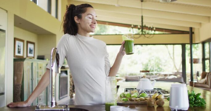 Happy biracial woman drinking smoothie in kitchen