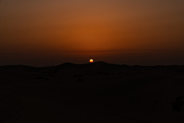 Sun setting above sand dunes in the desert