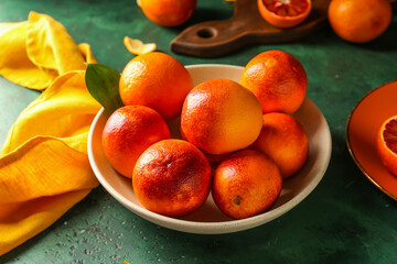 Bowl with tasty blood oranges on green background