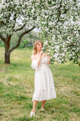 Fototapeta na wymiar beautiful woman walks in the spring garden. A girl in a white dress in blooming apple trees