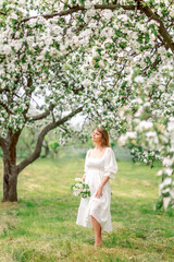 Fototapeta na wymiar girl in a white dress in a spring garden with a bouquet of flowers.