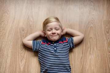 Cute happy smiled caucasian blond boy is laying on floor at home, copy space. Place for text