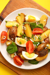 Plate of tasty potato salad with eggs and tomatoes on wooden board