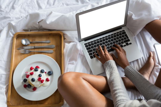 Low section of woman using laptop while sitting on bed at home
