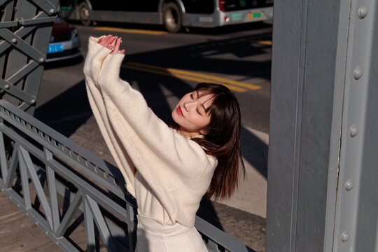 Beautiful young woman with black long hair in white skirt posing eyes closed on Shanghai garden bridge (Waibaidu bridge) in sunny day. Emotions, people, beauty, travel and lifestyle concept.