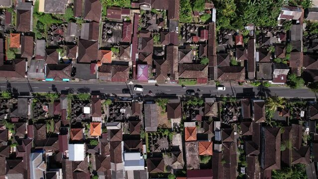 Panning aerial shot of Sebatu village, Gianyar regency of Bali Island. Plan view from drone, traditional house compounds build along straight road. Some vehicles ride at empty street