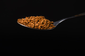 Close-up of instant granulated coffee in a teaspoon on a black background, macro photography