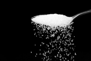 Obraz na płótnie Canvas Macro photography of a teaspoon with crumbling white sugar on a black background, copy space.