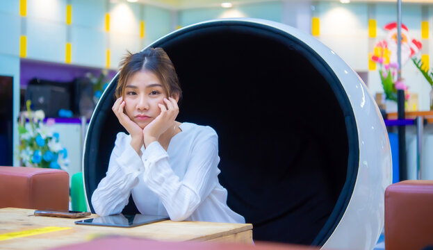 Beautiful Asian Business Woman Is Sitting On A Modern Round Chair With Sad Face On The Table Has A Phone And Tablet On It While Looking At The Camera, Digital Marketing.