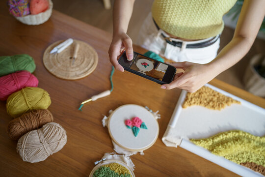 Asian Woman taking smartphone photo Punch needle. phone posting on social networks in studio workshop. designer workplace Handmade craft project DIY embroidery