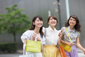 街中でスマートフォンを持ち微笑む女性3人