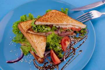 Breakfast sandwich toast with salad. Blue background. Bread, beakon tomatoe on plate top view. Meat sandwich. Sandwiches with ham, cheese, tomatoes, lettuce, and toasted bread. Healthy food.