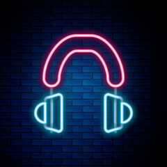 Glowing neon line Headphones icon isolated on brick wall background. Earphones. Concept for listening to music, service, communication and operator. Colorful outline concept. Vector