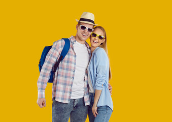Portrait of happy young couple of female and male tourists traveling abroad on weekend. Joyful active couple of travelers in casual clothes, sunglasses and with backpack on orange background.