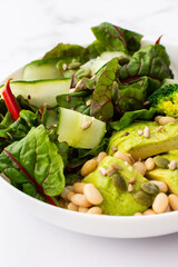 Healthy breakfasts, chard salad with beans and cucumbers, avocado and broccoli sprinkled with different seeds, a plate with food on a white marble background