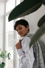 portrait of a pretty teenager standing near the window indoors and smiling at camera