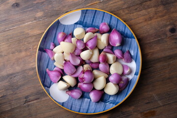 peeled shallots and peeled garlic in a ceramic plate with Asian motifs on a brown wooden table. herbs. bawang merah bawang putih kupas. 