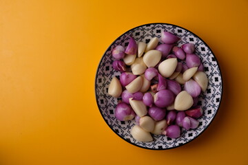 peeled shallots and peeled garlic in a ceramic plate with Asian motifs on a yellow table. herbs. bawang merah bawang putih kupas. 