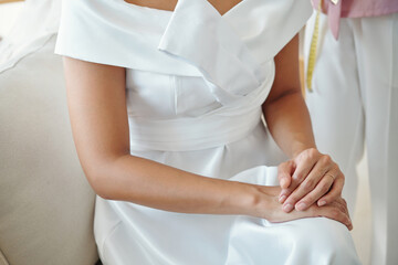 Fototapeta na wymiar Cropped image of bride in wedding dress sitting on couch in atelier