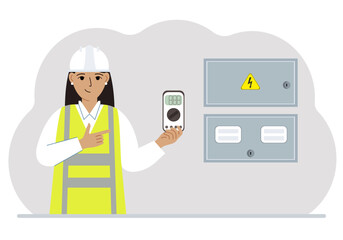 A female electrical engineer holds a digital multimeter in his hand and stands next to an electrical cabinet.