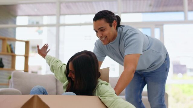 Moving in, box and a homeowner couple playing together in the living room of their new home with excitement. Property, love or happy with a playful man and woman having fun while bonding in a house