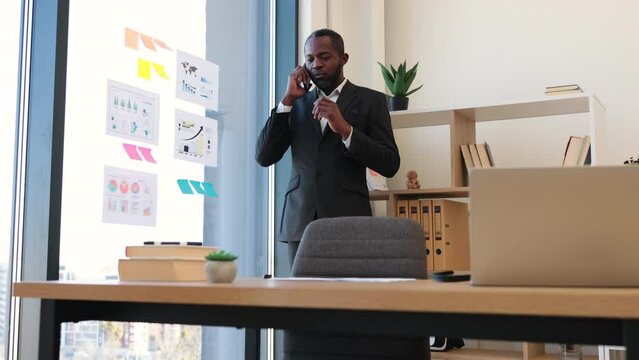 Thoughtful multicultural man in business suit speaking on mobile phone while waiting for meeting in conference hall. General manager frowning heavily while concentrating on conversation over gadget.