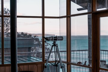 View of a modern telescope placed by the windows in a waterside building