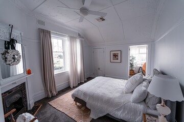 High angle of the bright bedroom with a white bed, a fireplace, a wall picture, and a bedside lamp