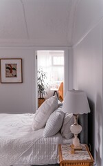 Bedroom with a white bed, a bedside lamp, and a wall picture next to the room with a big green plant