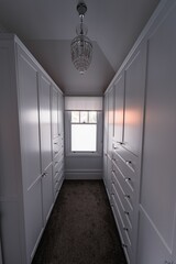 Vertical shot of a dressing room with white drawers and wardrobes