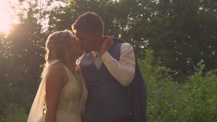 LENS FLARE, PORTRAIT: Romantic kiss of newlyweds in beautiful golden sunlight. Candid romantic moments between beautiful bride and groom on their wedding day. Cute married couple in warm sunset light.