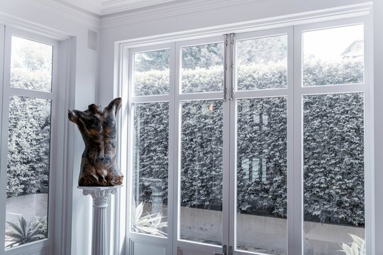 Bronze nude figural body sculpture placed on a marble column by the windows