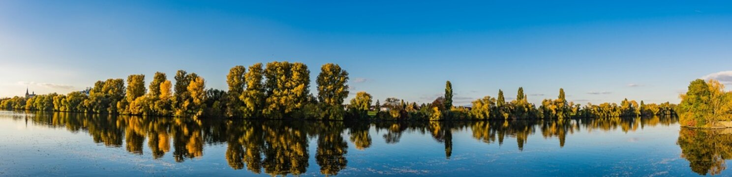Panoramic shot of the reflection of the trees in the lake at sunset in Raunheim, Germany.