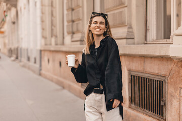 Smiling beautiful stylish woman having good fashion clothes walking on street and holding some coffee in cup takeaway with good summer mood. Girl look happy, turn around or spinning.