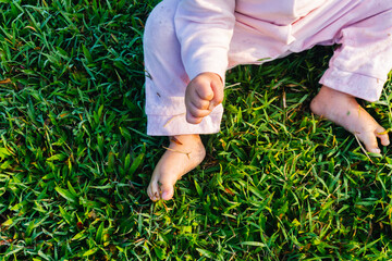 unrecognizable child's hand and feet sit on green grass playing with grass with pajamas in the morning