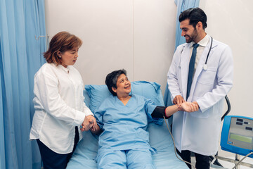 Obraz premium Hospitalized woman lying in bed while doctor checking his pulse. Doctor examining senior female patient in hospital room.