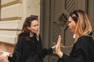 Quarrel two friends. Two women screaming at each other. Two young women argue near door outdoor on the street. Family problem. Angry female show emotion. Depression people. Stress family photo.