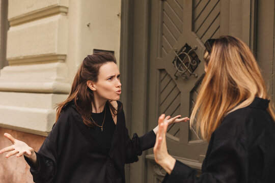 Quarrel two friends. Two women screaming at each other. Two young women argue near door outdoor on the street. Family problem. Angry female show emotion. Depression people. Stress family photo.