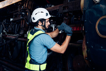 Male engineer maintenance locomotive engine wearing safety uniform, helmet and gloves work in locomotive repair garage. 