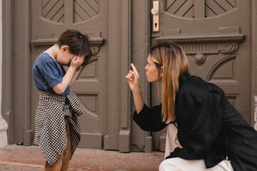 Mother scolds her son on the street. Child cries, a woman shakes her finger because of the boy bad...