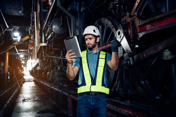 Fototapeta na wymiar Portrait of professional man engineer in white hardhat standing and holding tablet working in train factory.