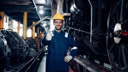 Male engineer worker maintenance locomotive engine wearing safety uniform, helmet and gloves in locomotive repair garage. Maintenance cycle concept.