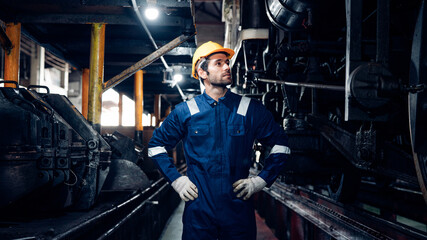 Male engineer worker maintenance locomotive engine wearing safety uniform, helmet and gloves in locomotive repair garage. Maintenance cycle concept.