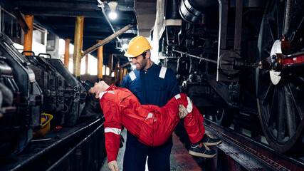 Mature foreman in workwear giving first aid to staff suffering after working injury in locomotive repair garage. Injury at work. 