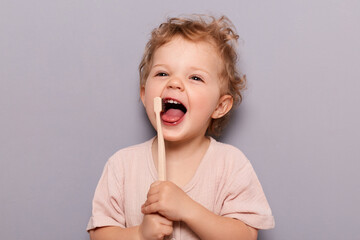 Portrait of laughing happy cheerful infant girl kid with curly blonde hair brushing her teeth,...
