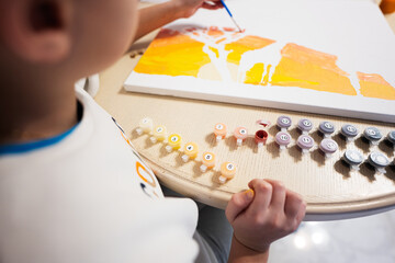 Left handed boy is painting by numbers with gouache at home.